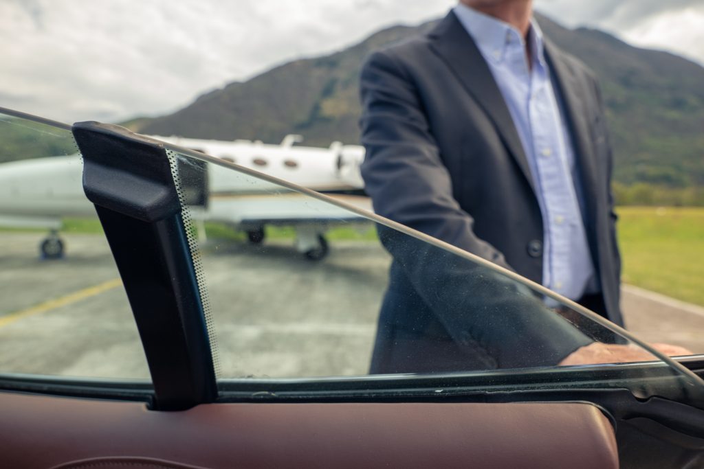 Professional chauffeur opening a luxury car door next to a private jet, highlighting a premium NYC airport chauffeur service for executive travelers
